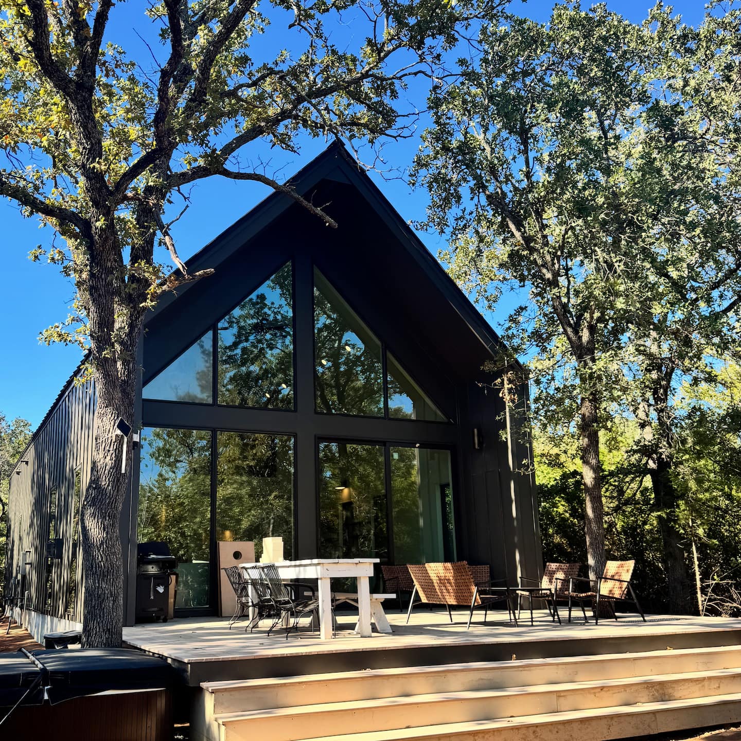 The cabin exterior in daylight with deck, dining, and hot tub